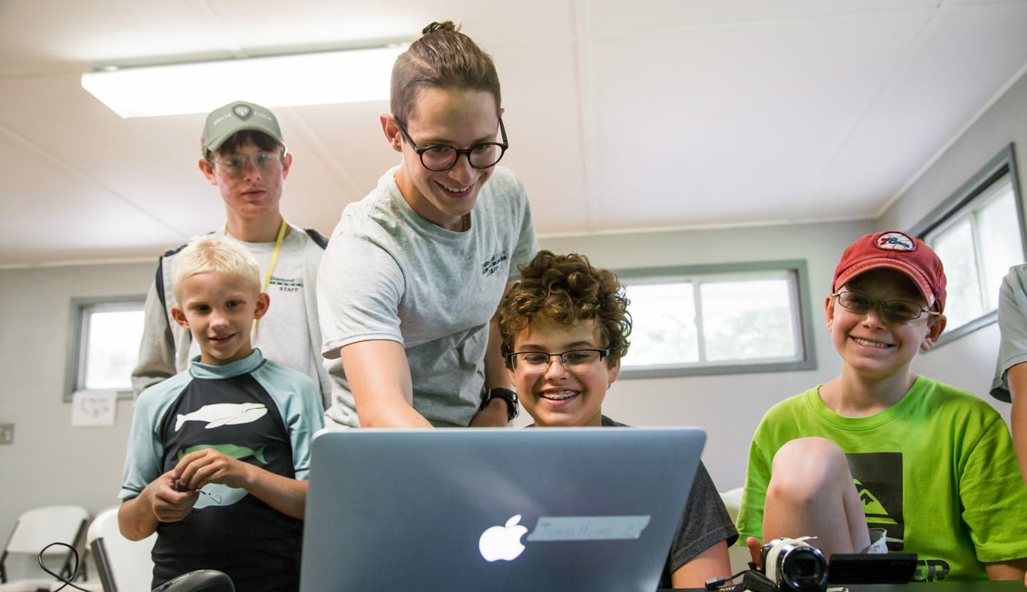 Senior counselor helping campers with media