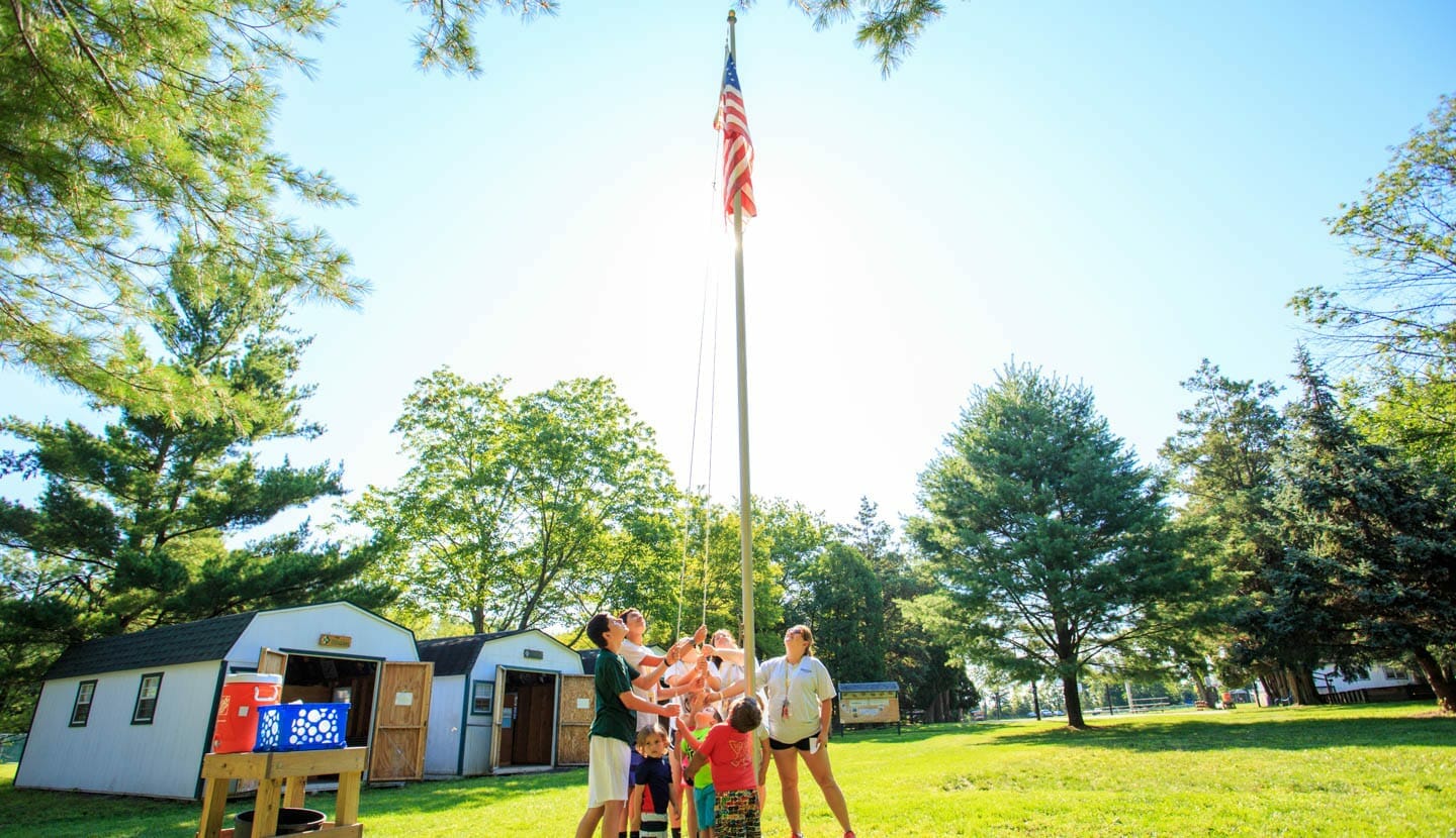 Junior counselors helping campers raise flag